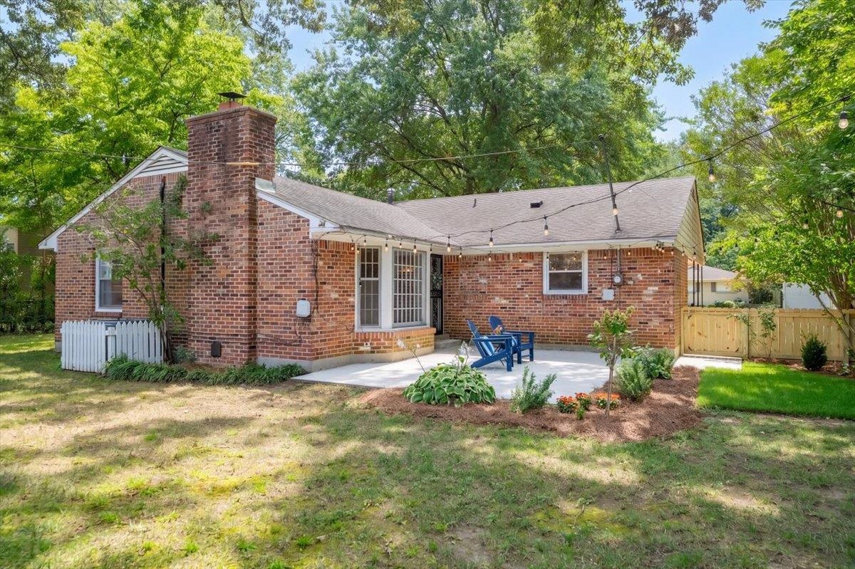 Brick home’s backyard patio with blue chairs, string lights, and mature trees.