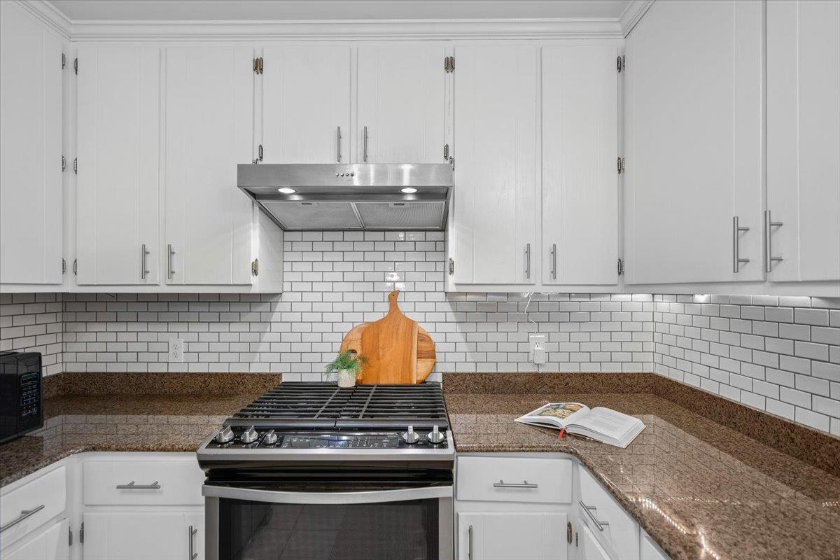 Kitchen with white cabinets, subway tile backsplash, granite counters, and a stainless steel gas range.