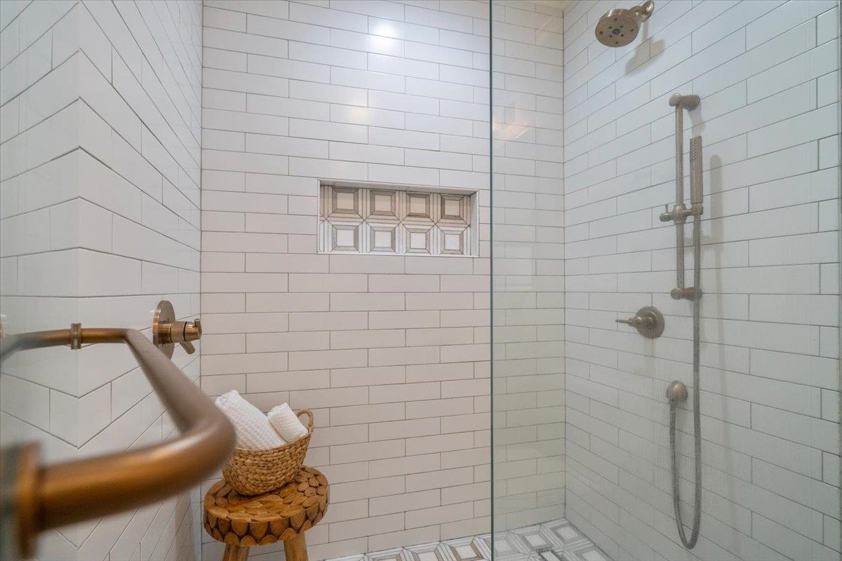 Walk-in shower with white subway tile, brass fixtures, glass enclosure, and recessed wall niche.