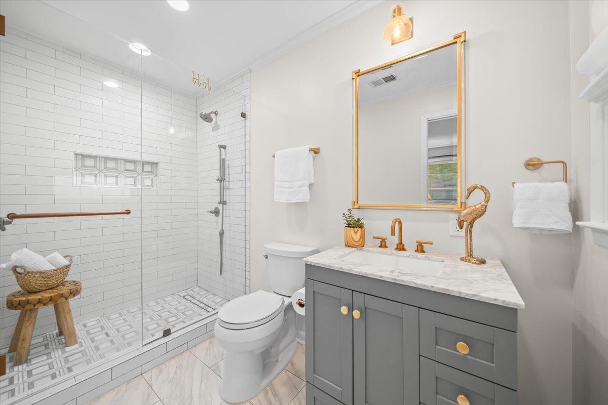 Bathroom with a glass-enclosed subway-tile shower and gray vanity with gold fixtures.