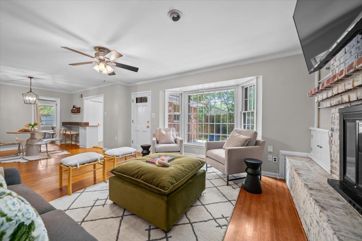 Living room with a bay window, brick fireplace, hardwood floors, and adjoining dining area.