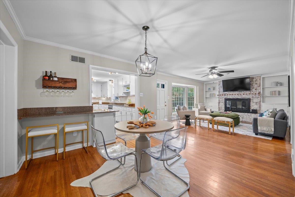 Open-plan dining and living area with a round table, hardwood floors, and brick fireplace.