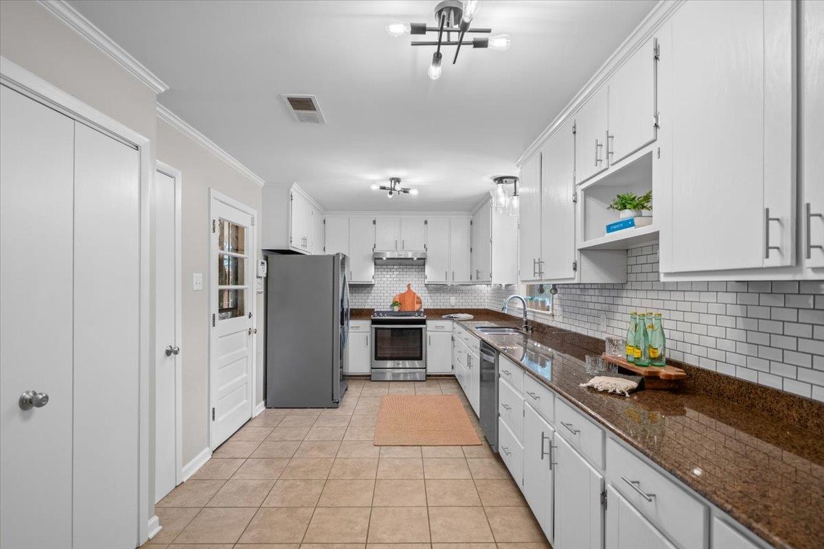 Long kitchen with white cabinetry, granite counters, subway tile backsplash, and stainless steel appliances