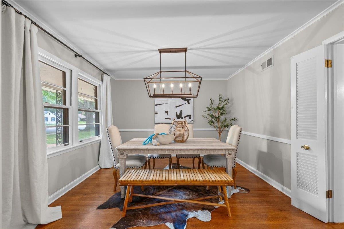 Dining room with a pale wood table, wooden bench, hardwood floors, and a geometric pendant light.