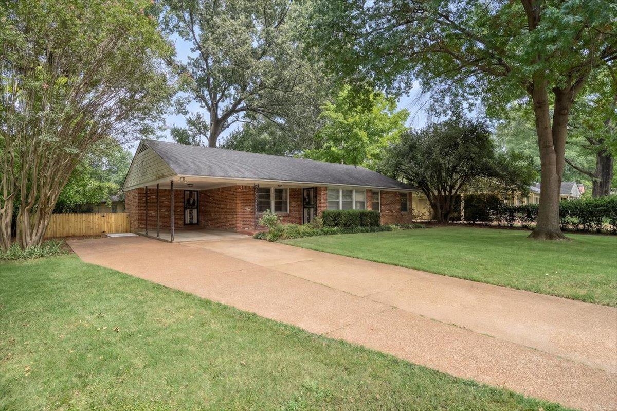 Single-story brick house with a covered carport, wide driveway, and mature trees.