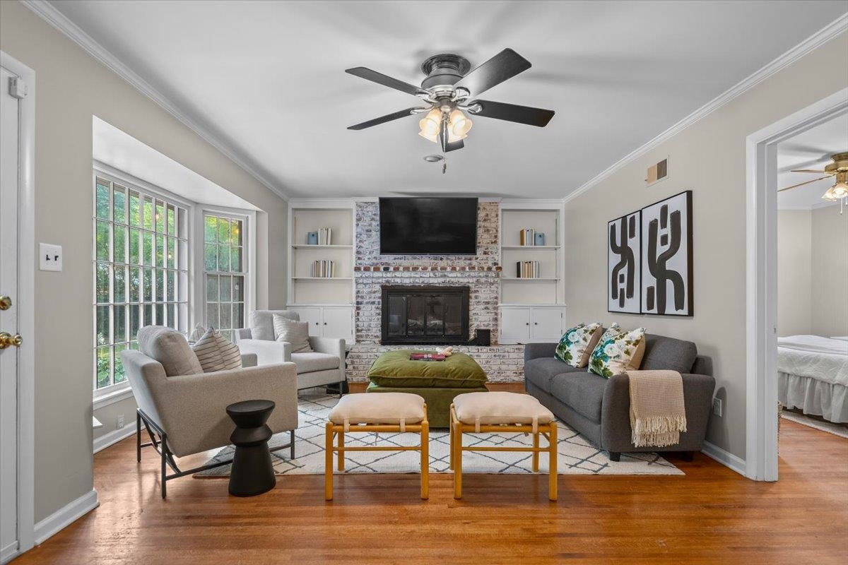 Living room with a brick fireplace, built-in shelves, large windows, and gray and cream seating.