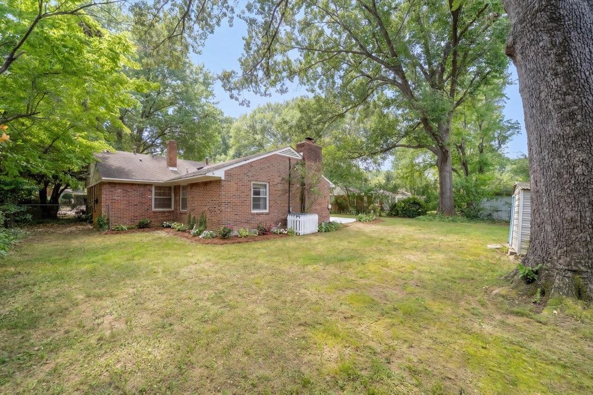 Brick house with a broad backyard lawn, mature shade trees, and a small white fence.