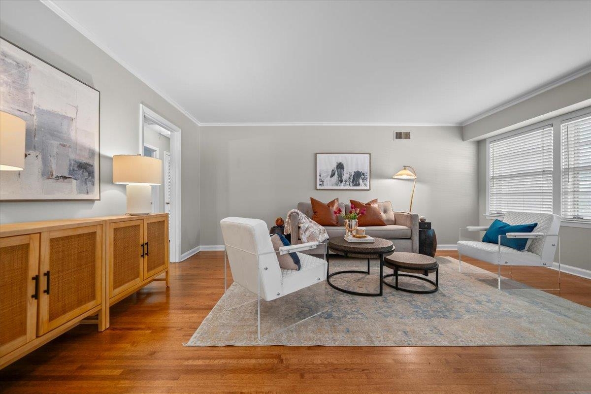Staged living room with a gray sofa, white chairs, round coffee tables, and hardwood floors.