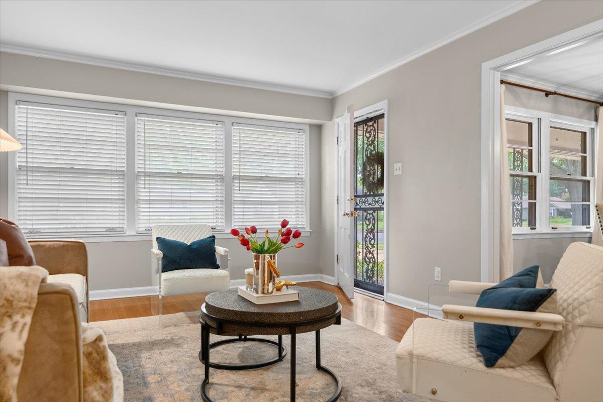 Living room with wide blinded windows, a decorative iron-and-glass door, and a round coffee table.