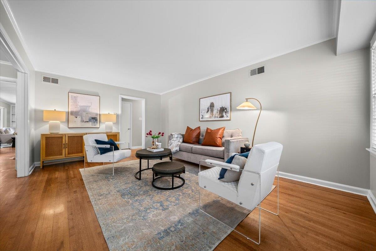 Staged living room with a gray sofa, white armchairs, hardwood floors, and a patterned rug.