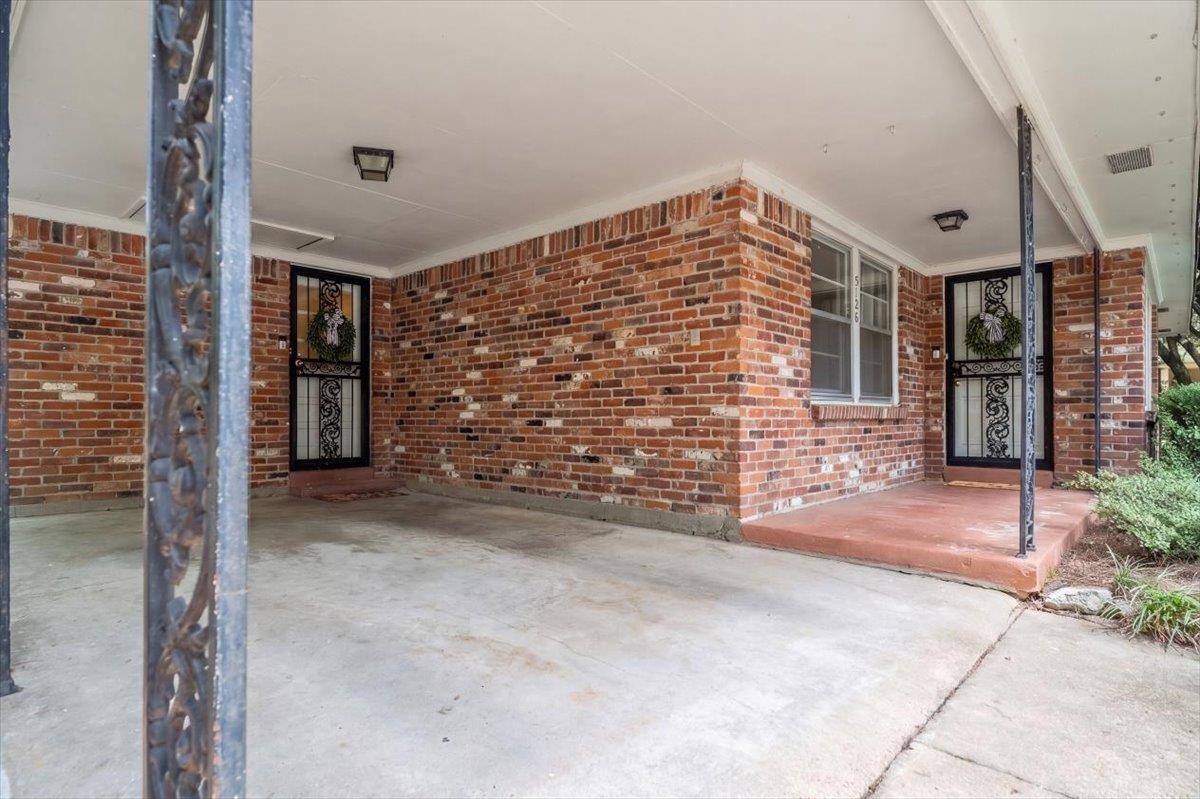 Brick home’s covered front porch with decorative security doors and a concrete driveway.