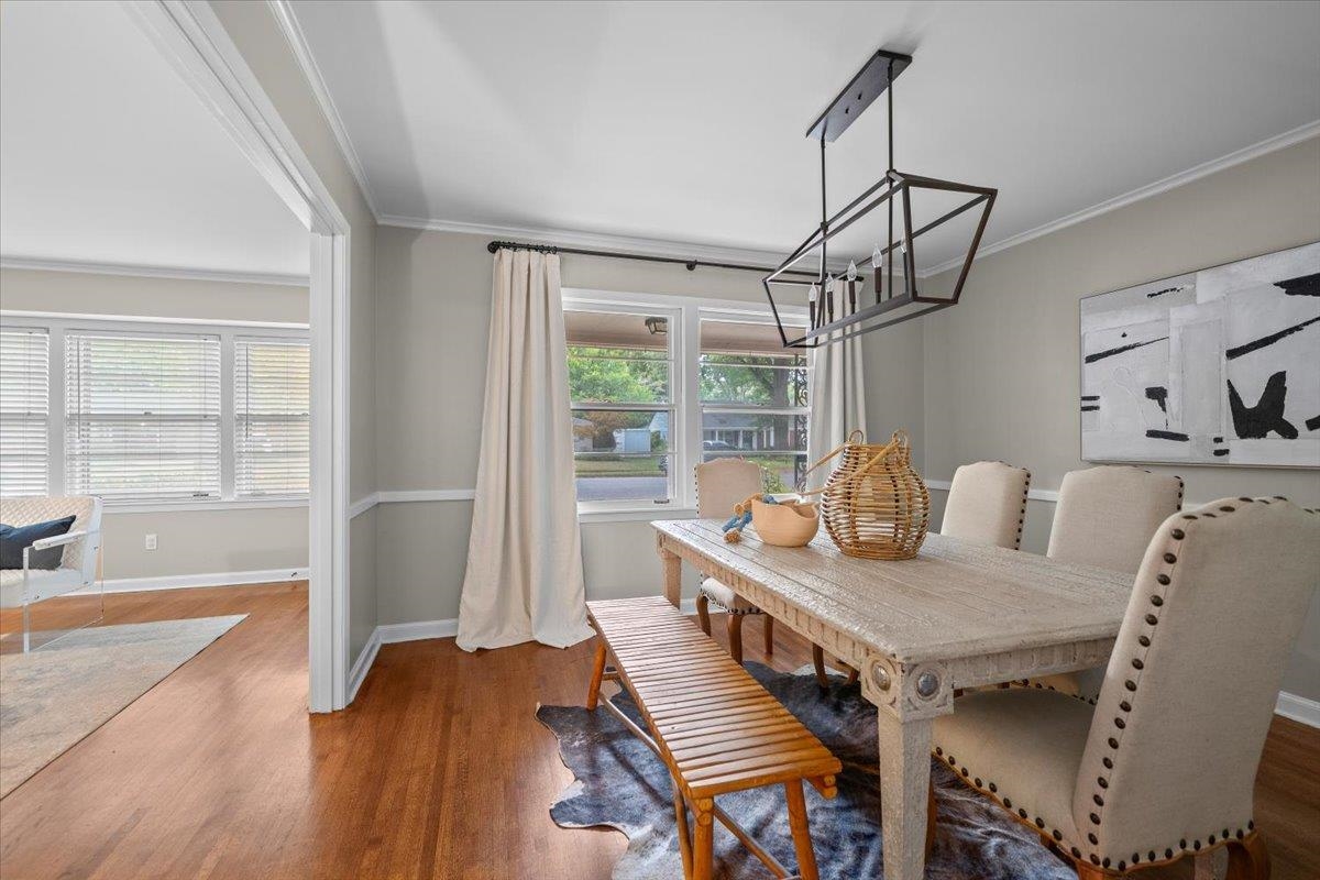 Dining room with a long wood table, upholstered chairs, geometric chandelier, and large street-facing windows.