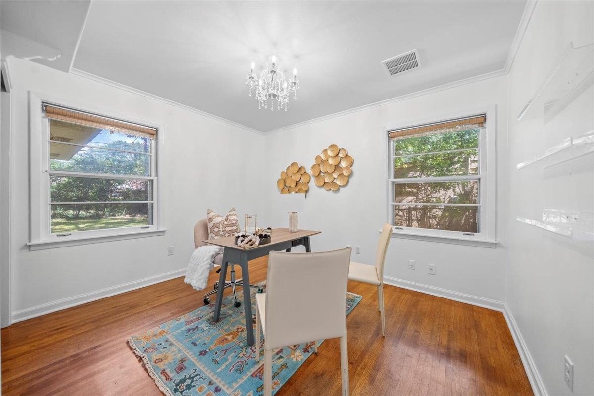 Dining room with a chandelier, patterned rug, hardwood floors, and windows overlooking greenery.