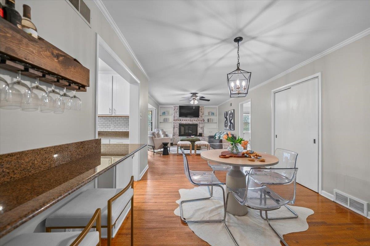 Open-plan dining room with a round table, granite kitchen counters, and a brick fireplace in the living room.