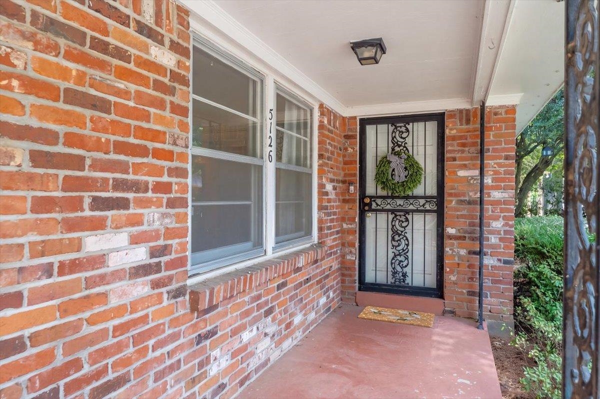 Brick home entry with a black decorative security door, wreath, and number 5126.