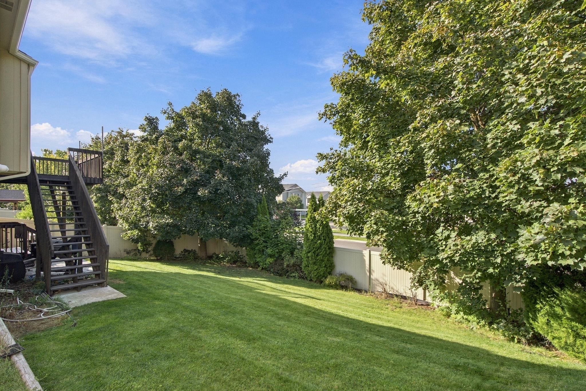 Backyard lawn with mature trees, privacy fencing, and stairs to a raised deck.