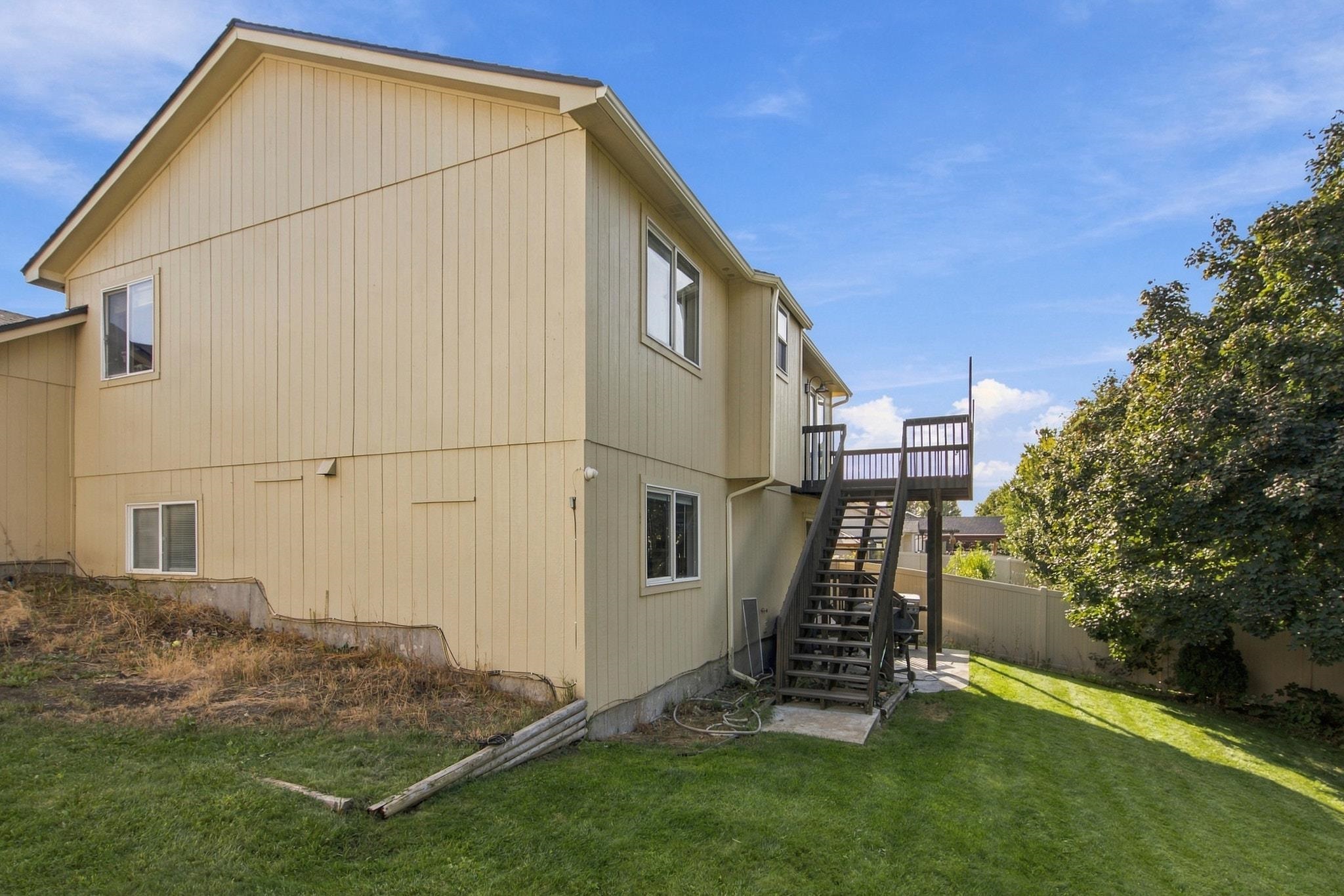 Two-story beige home with a raised deck and stairs overlooking a fenced backyard.