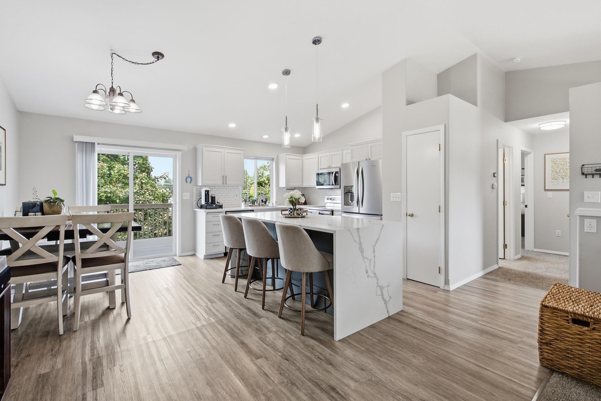 Open-plan kitchen and dining area with a marble-look island, stainless appliances, and sliding glass door to the deck.