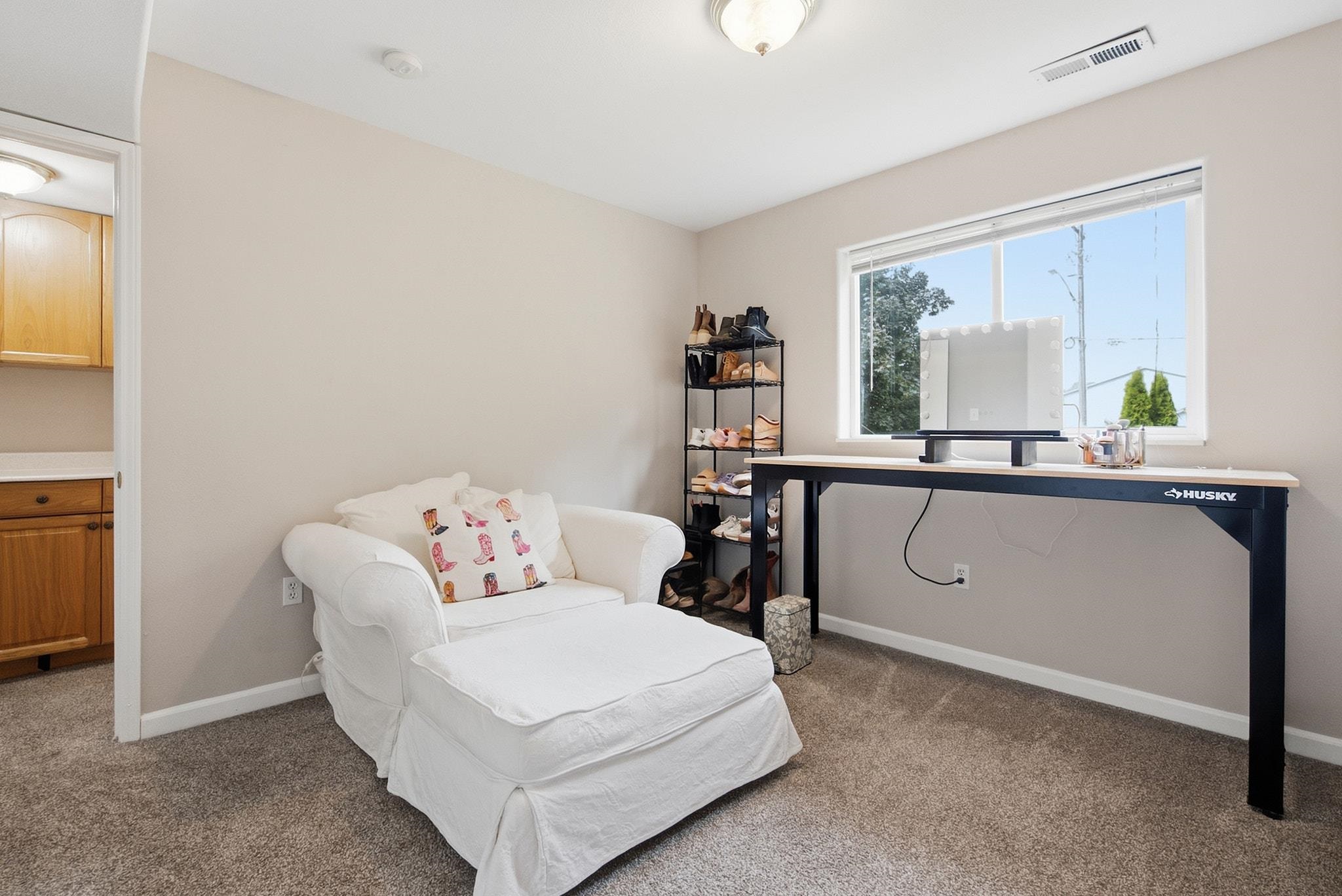 Furnished dressing room with a white chaise, makeup table, large window, and shoe rack.