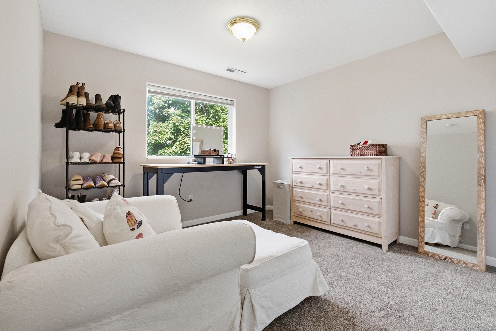 Furnished bedroom with a white sofa bed, shoe rack, desk, pale dresser, and full-length mirror.