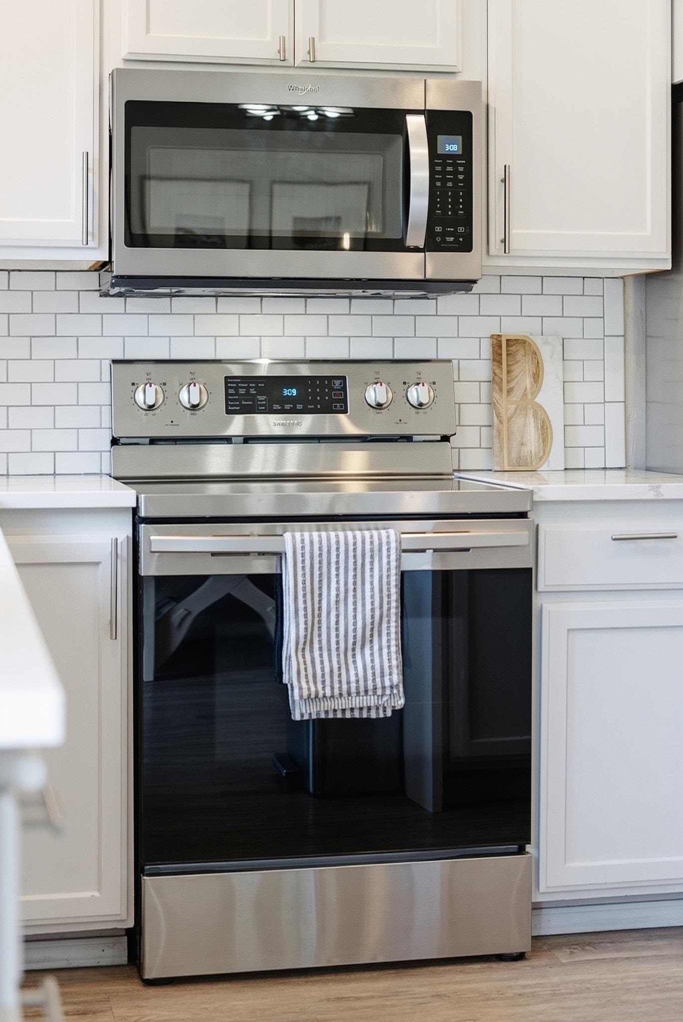 Kitchen with stainless steel microwave and range, white cabinetry, subway tile backsplash, and striped oven towel.