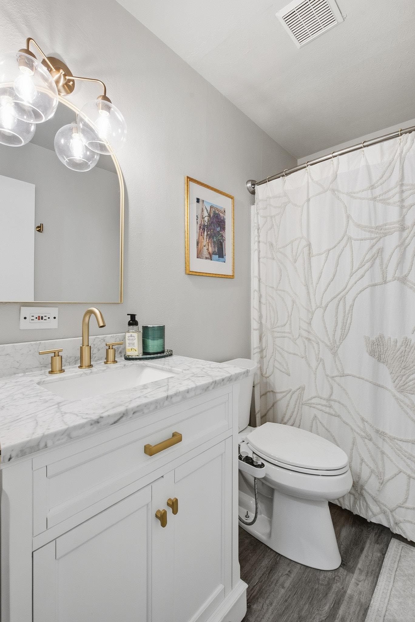 Bathroom with marble-topped white vanity, brass fixtures, and a patterned shower curtain.