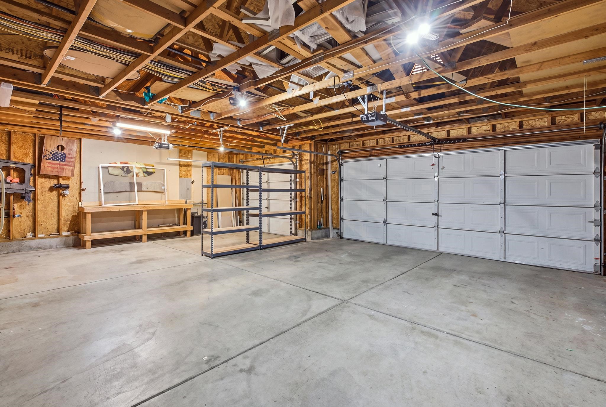 Spacious garage with two white doors, exposed ceiling framing, concrete floor, workbench, and metal shelving.