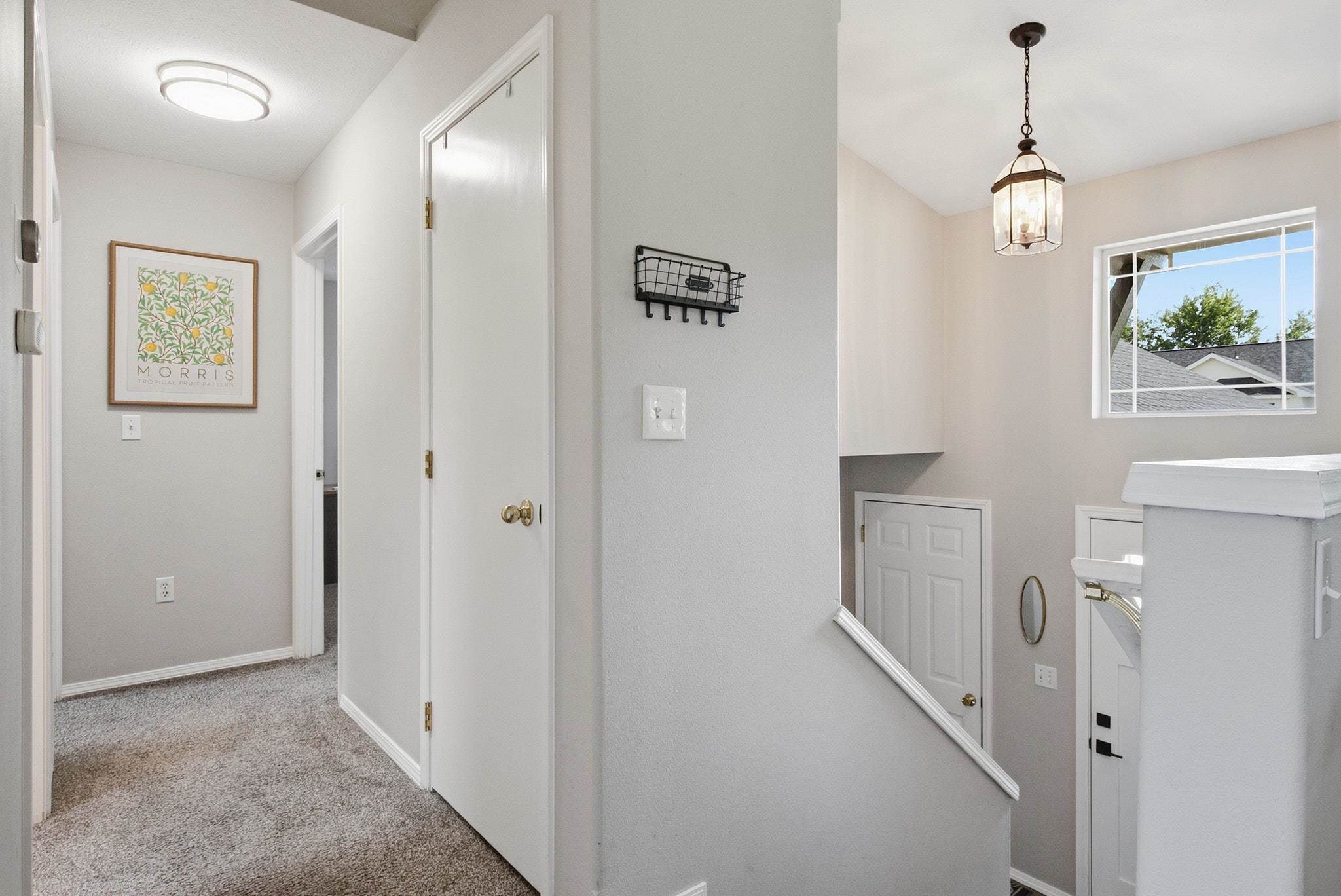 Carpeted upstairs hallway and stair landing with a pendant light and a window overlooking rooftops.