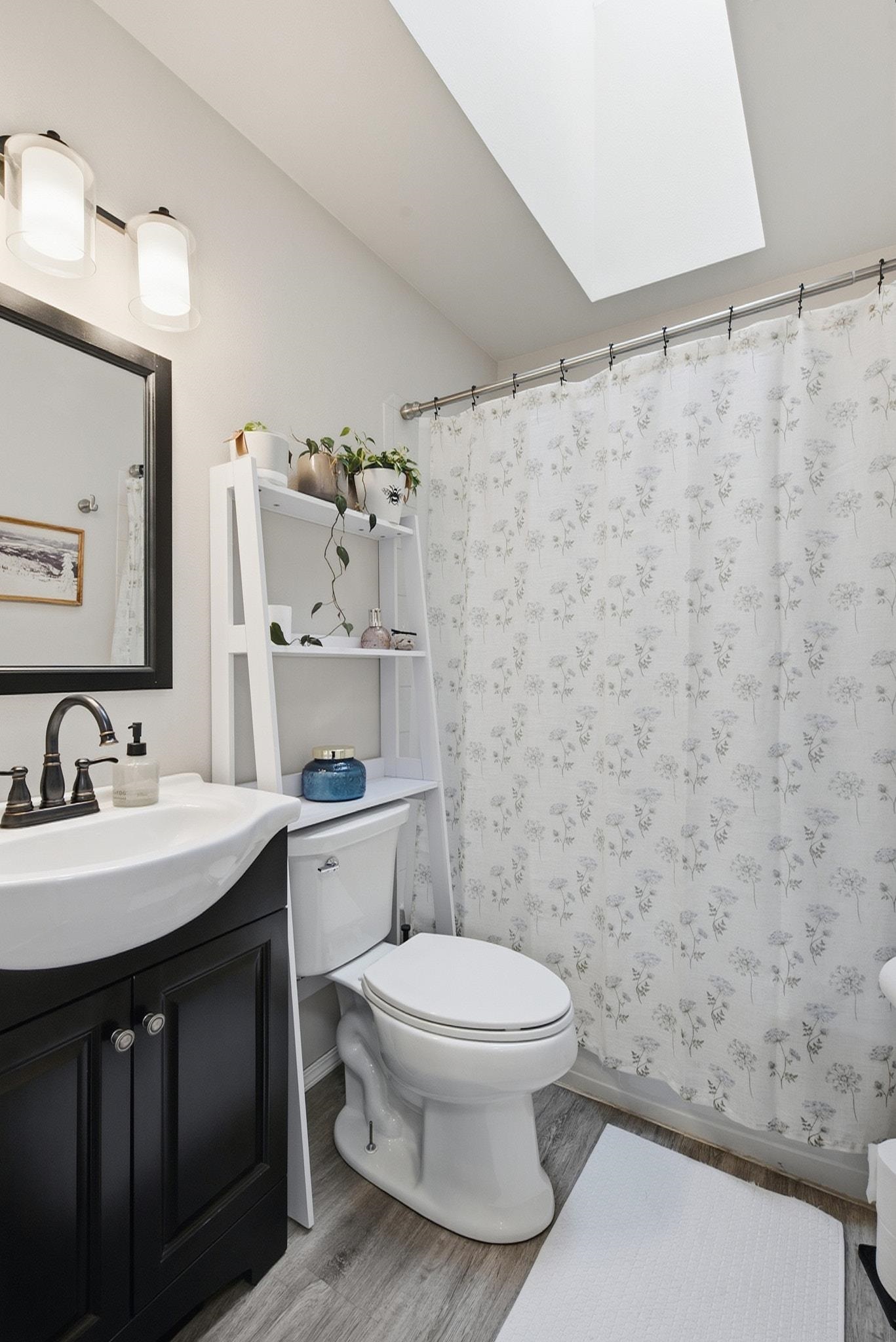 Bathroom with a floral shower curtain, skylight, and dark vanity.