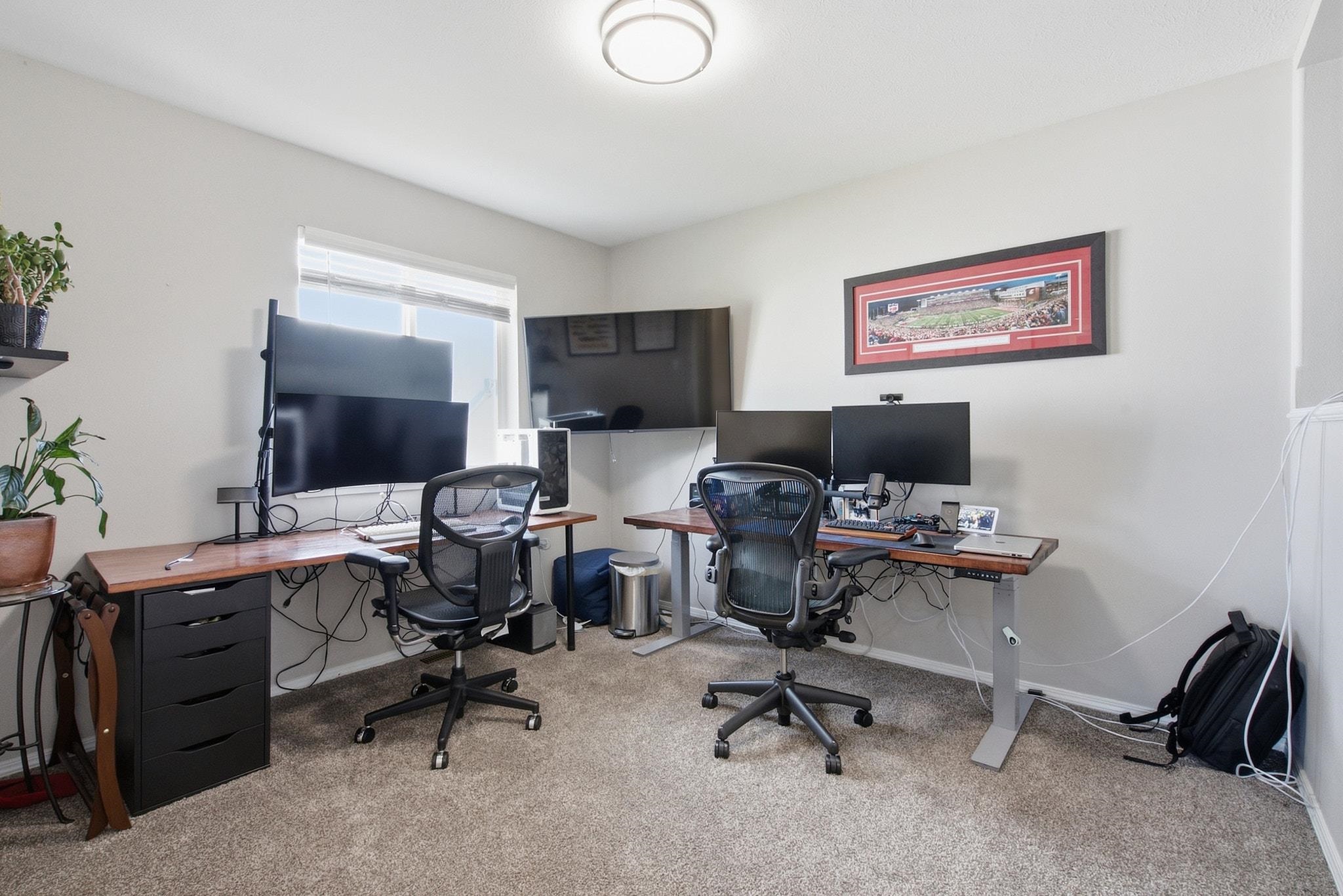 Home office with two computer workstations, ergonomic chairs, and framed stadium art.