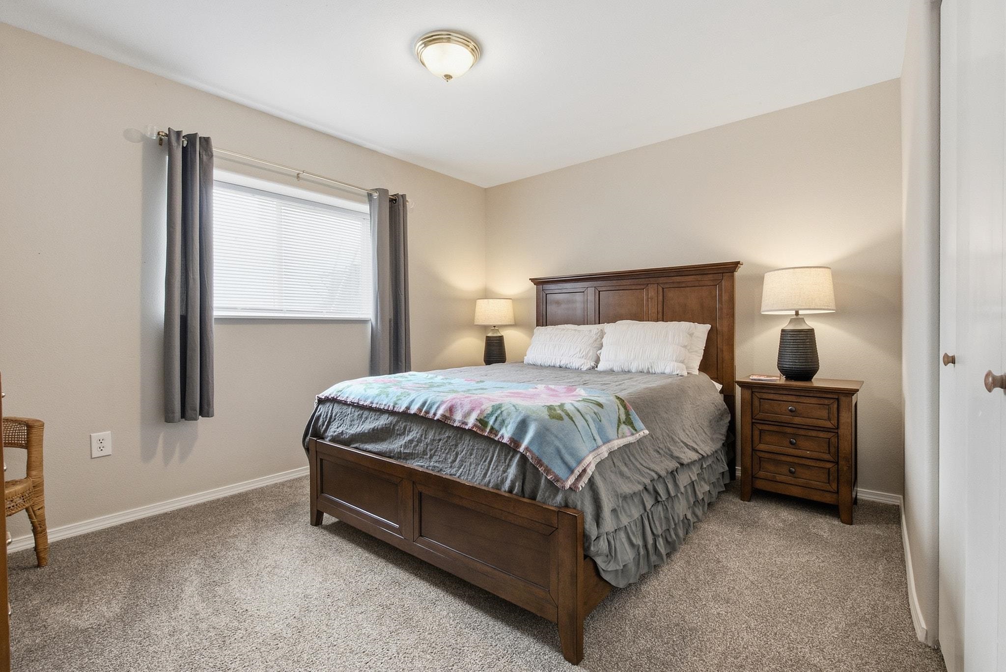 Bedroom with a dark wooden bed, gray bedding, colorful quilt, and window with gray curtains.