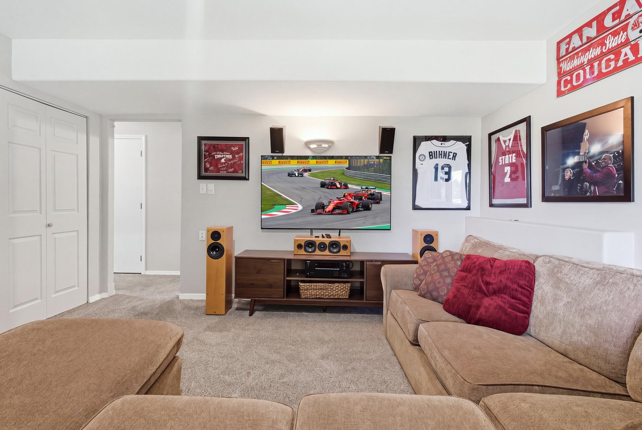 Media room with a large television, surround-sound speakers, beige sectional, and framed sports memorabilia.