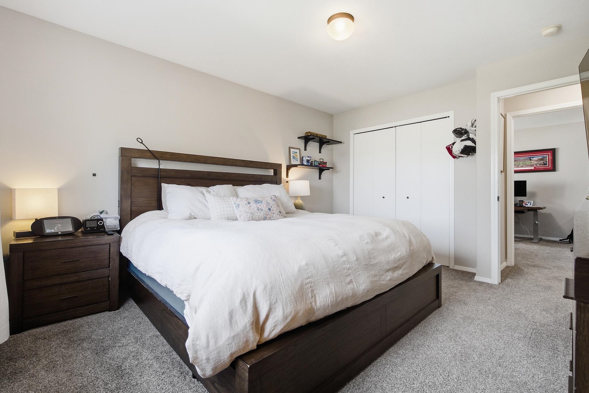 Bedroom with a dark wood platform bed, white bedding, and sliding closet doors beside an open doorway to an office.