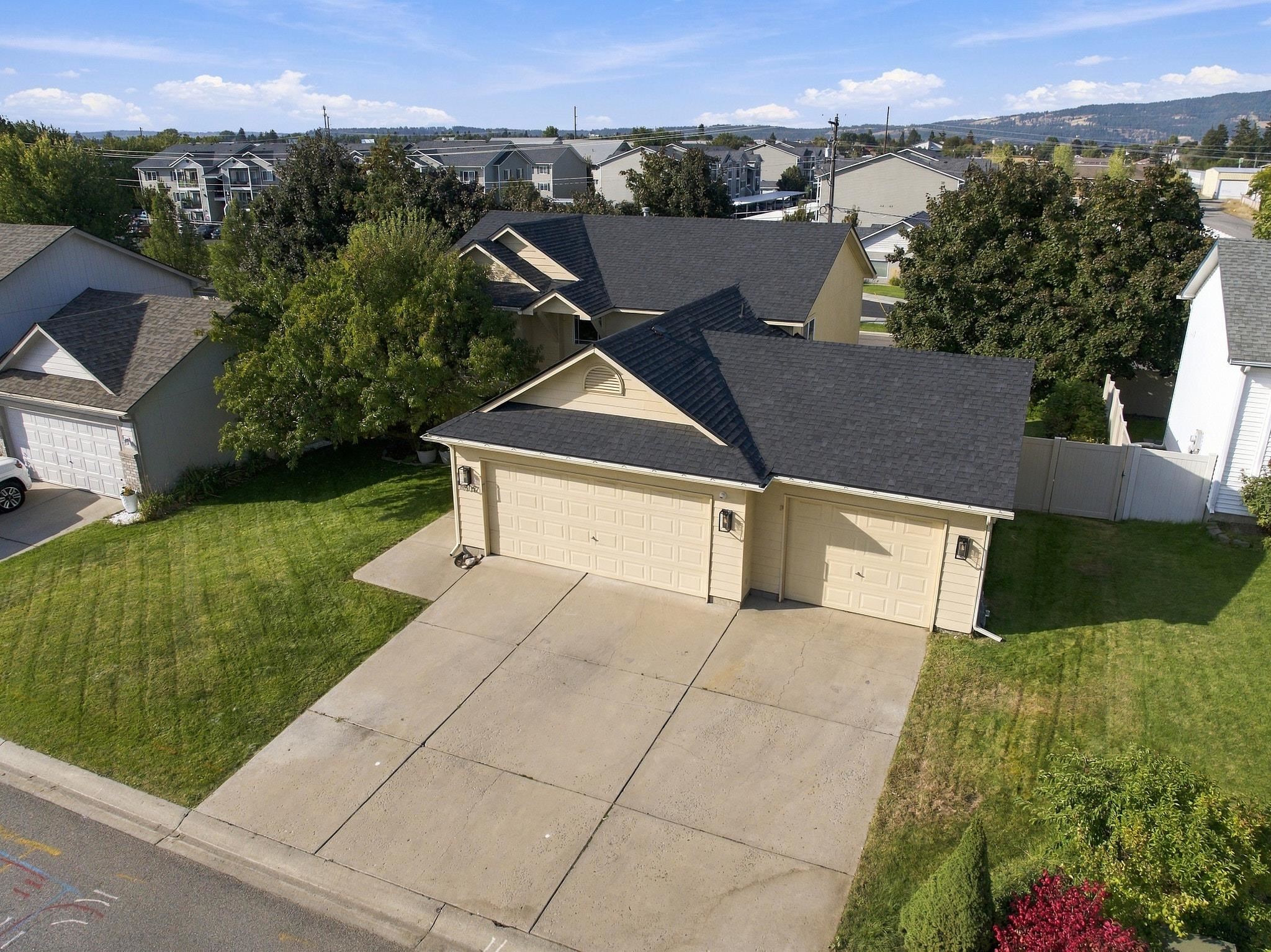 Aerial view of a tan home with two garage doors, a wide driveway, and a front lawn.