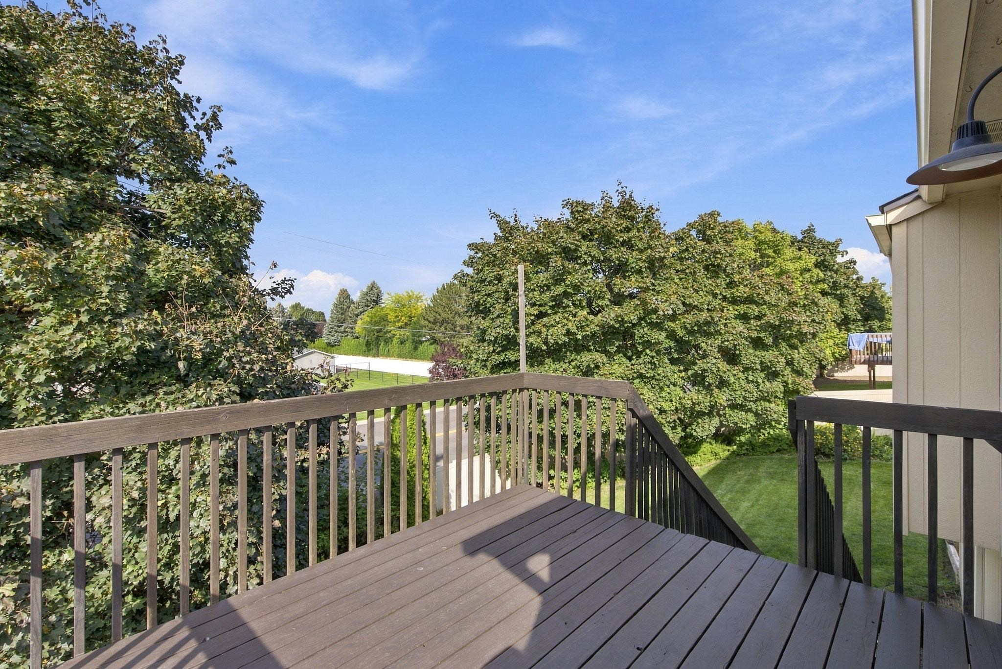 Raised wood deck overlooking a leafy backyard, with dark railings and a sunny blue sky.