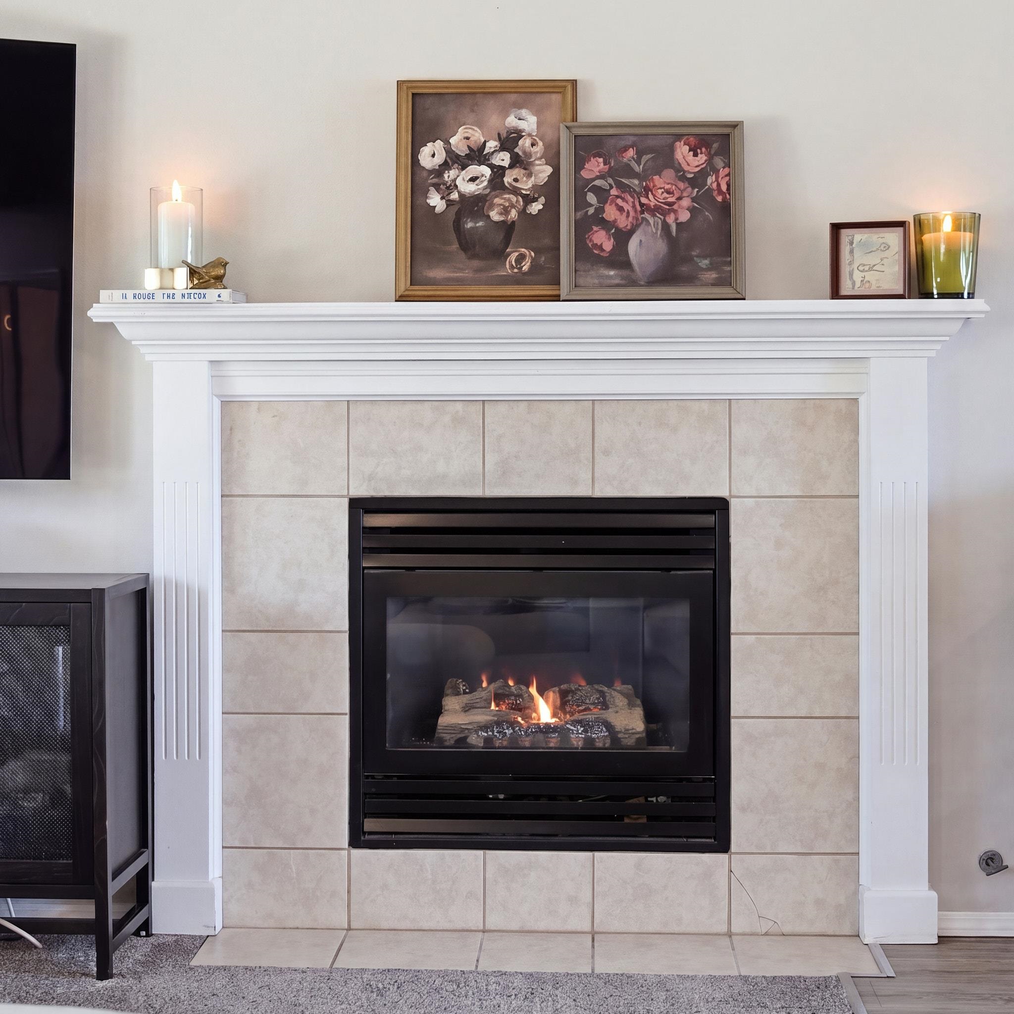 Living room fireplace with a black gas insert, pale tile surround, and white mantel topped with floral artwork.