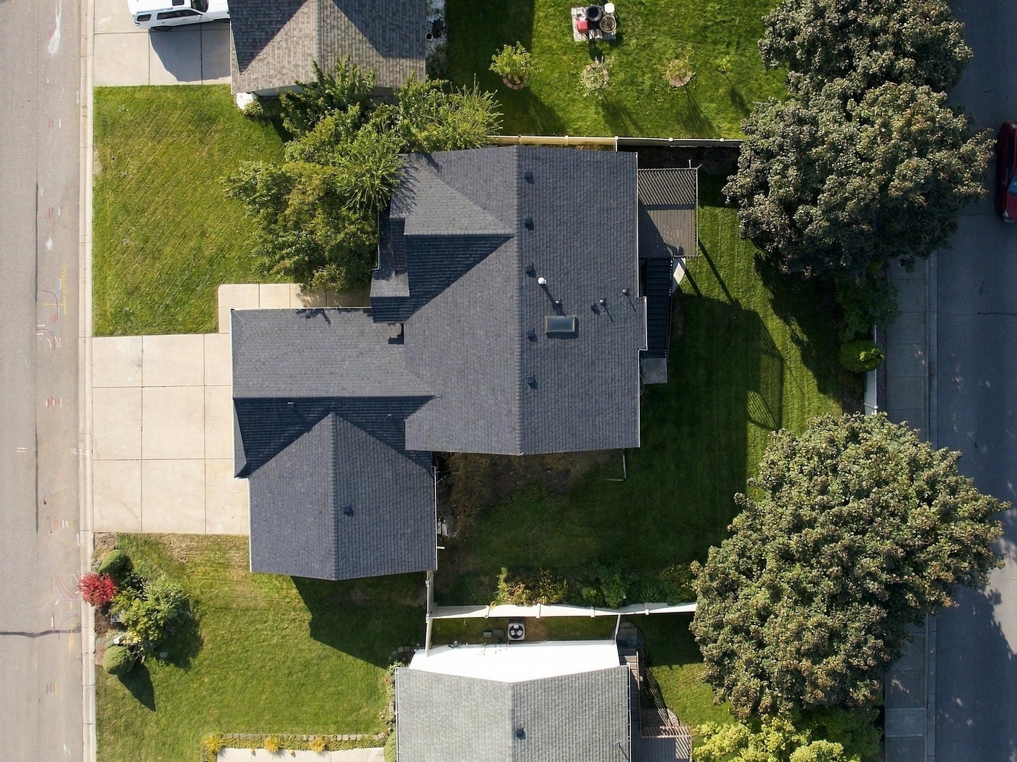 Aerial view of a gray-roofed house with a broad lawn, mature trees, and concrete driveway.