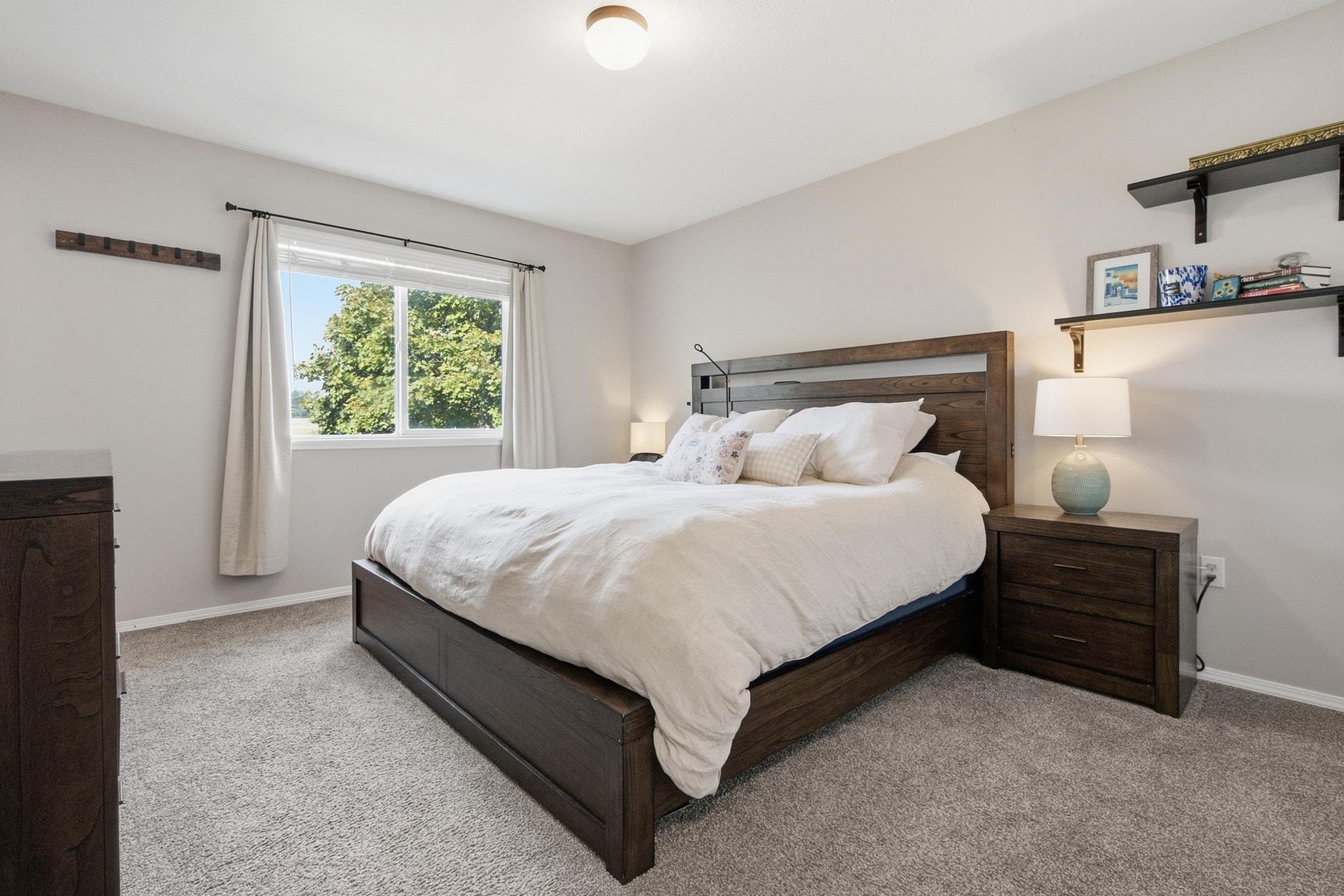Furnished bedroom with a dark wood bed, white bedding, and a large curtained window.