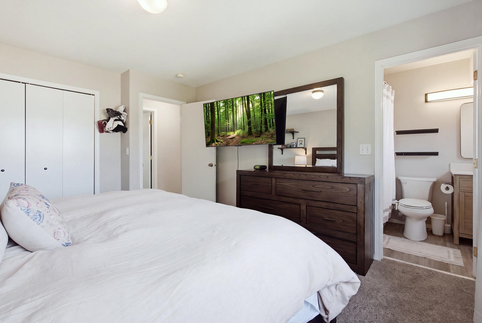 Bedroom with a white bed and dark wood dresser, opening onto an adjoining bathroom.