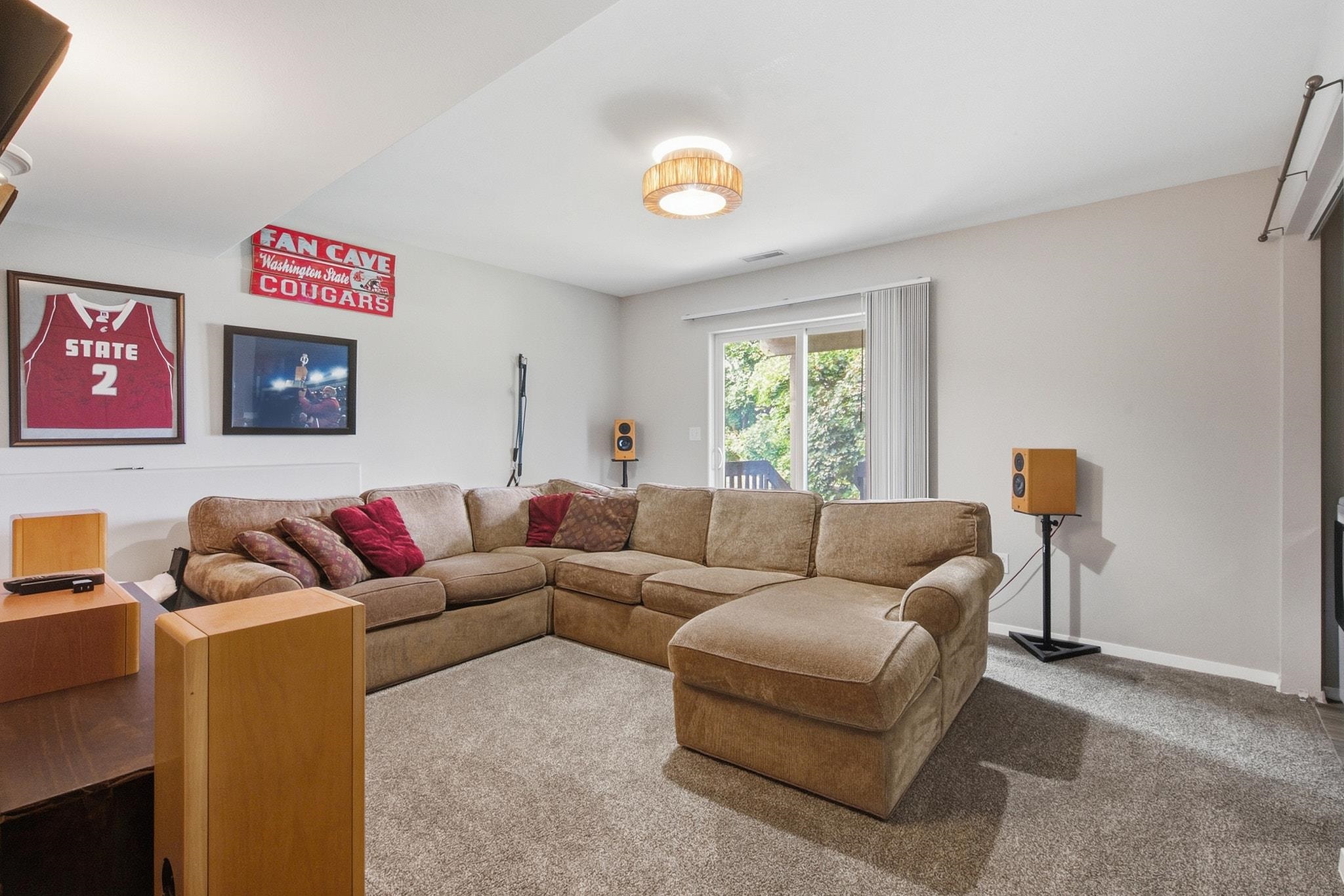 Furnished living room with a tan sectional, speaker cabinets, and Washington State Cougars decor.