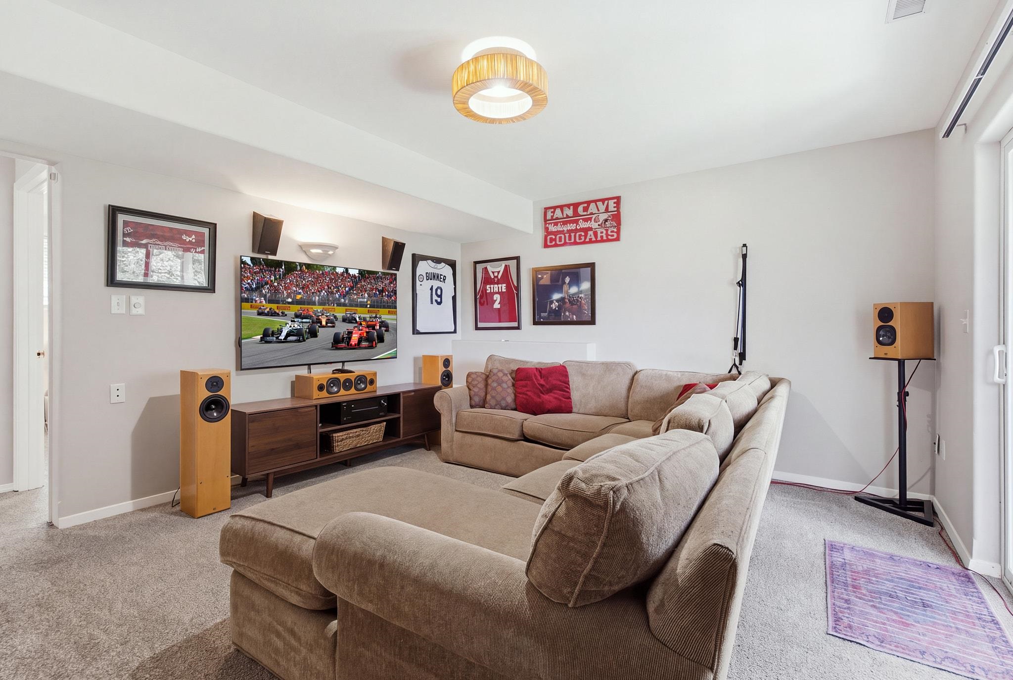 Furnished media room with a large sectional, surround-sound speakers, and sports memorabilia.