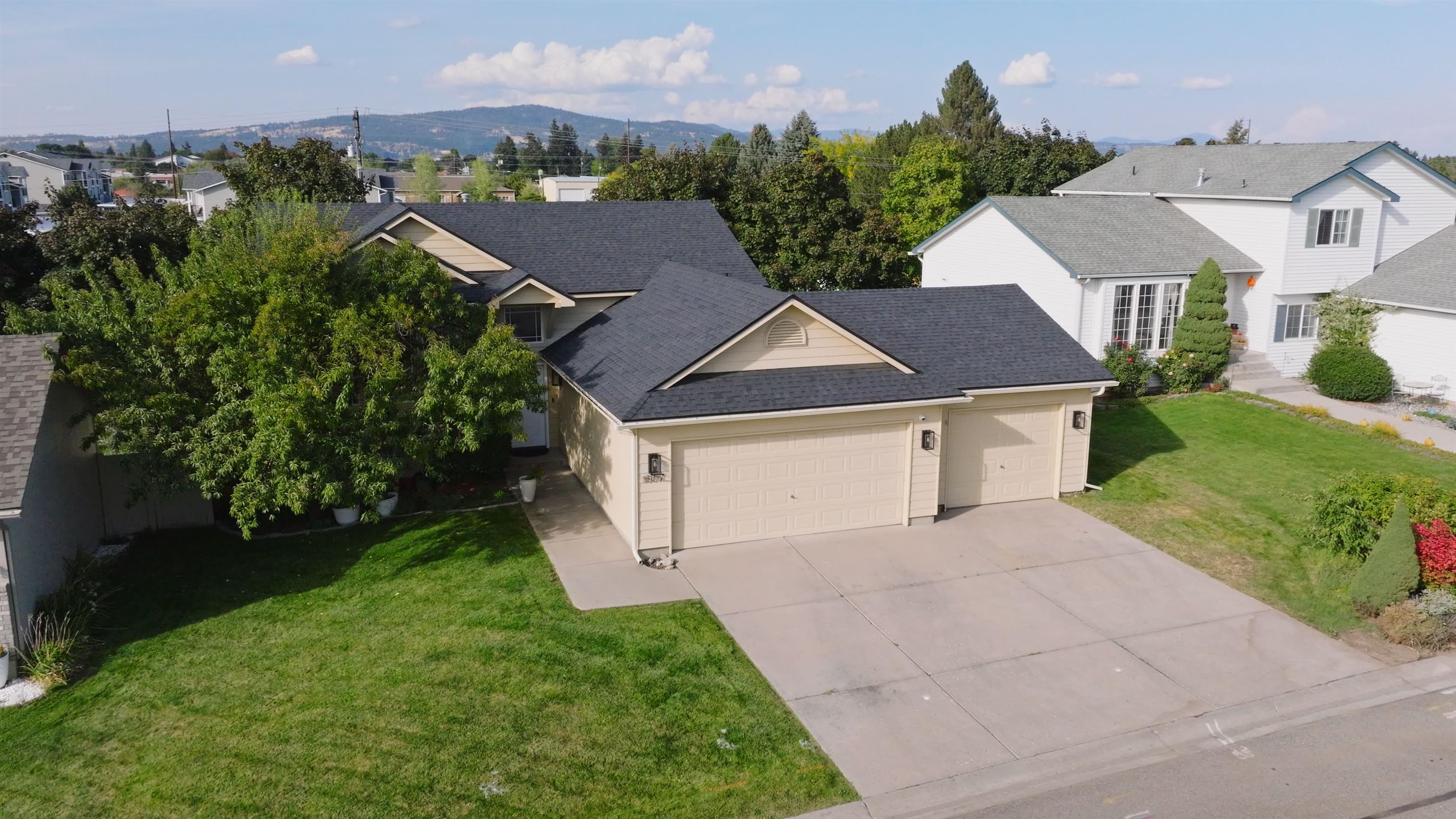 Tan home with a dark roof, two-car garage, wide driveway, and landscaped lawn, viewed from above.