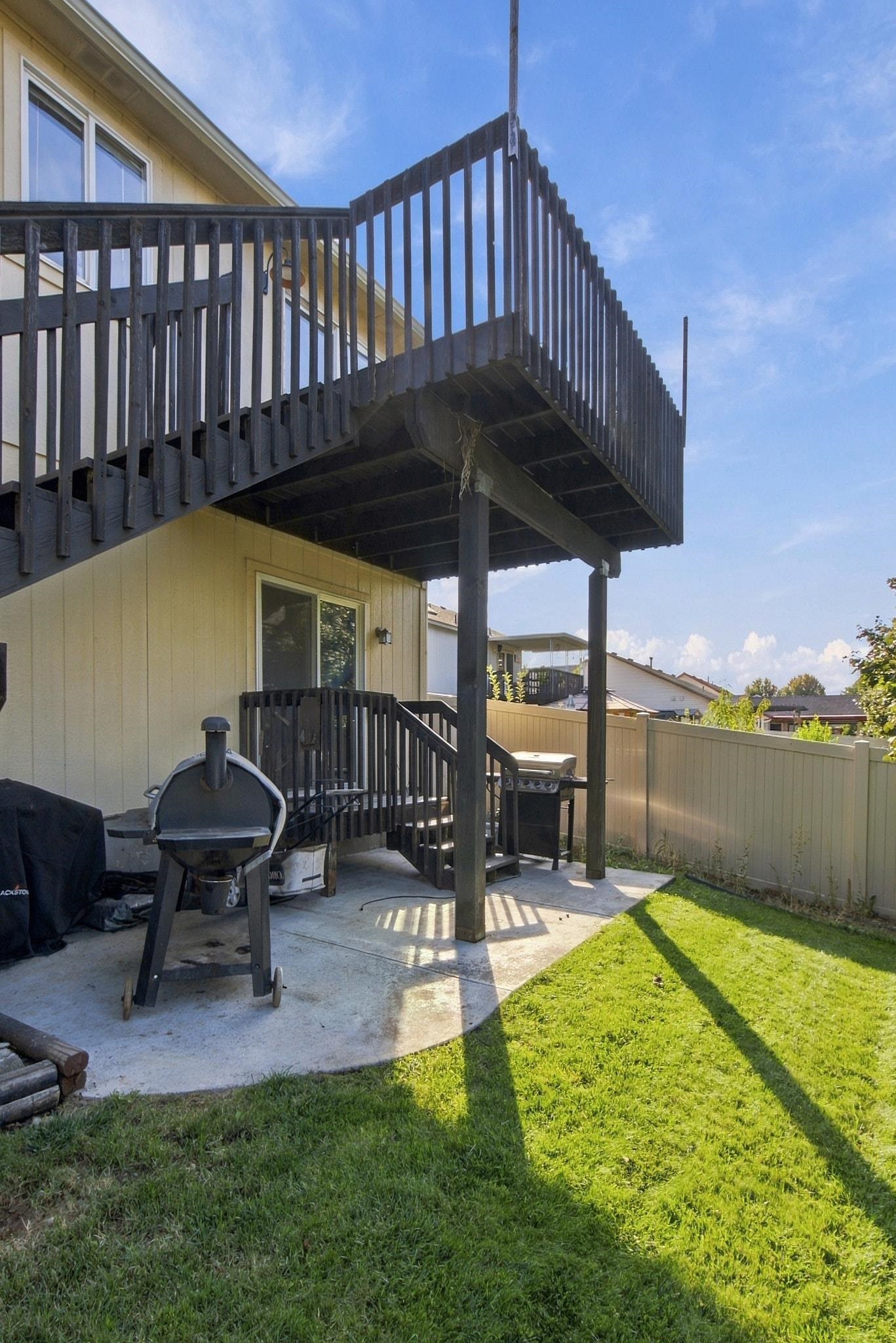 Backyard patio with an elevated black deck, grill, concrete pad, and fenced lawn.
