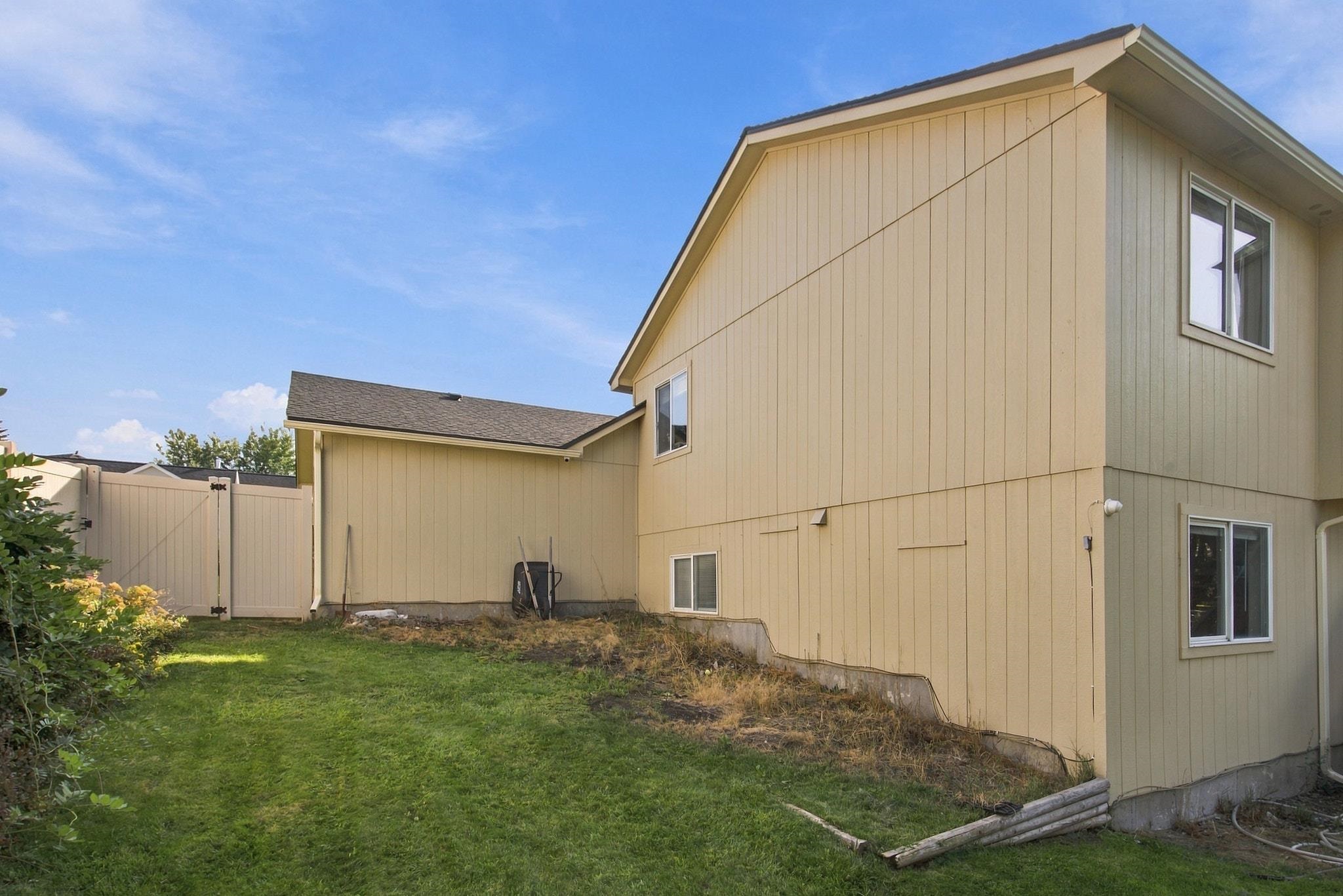 Two-story beige home beside a grassy yard and tall privacy fence.