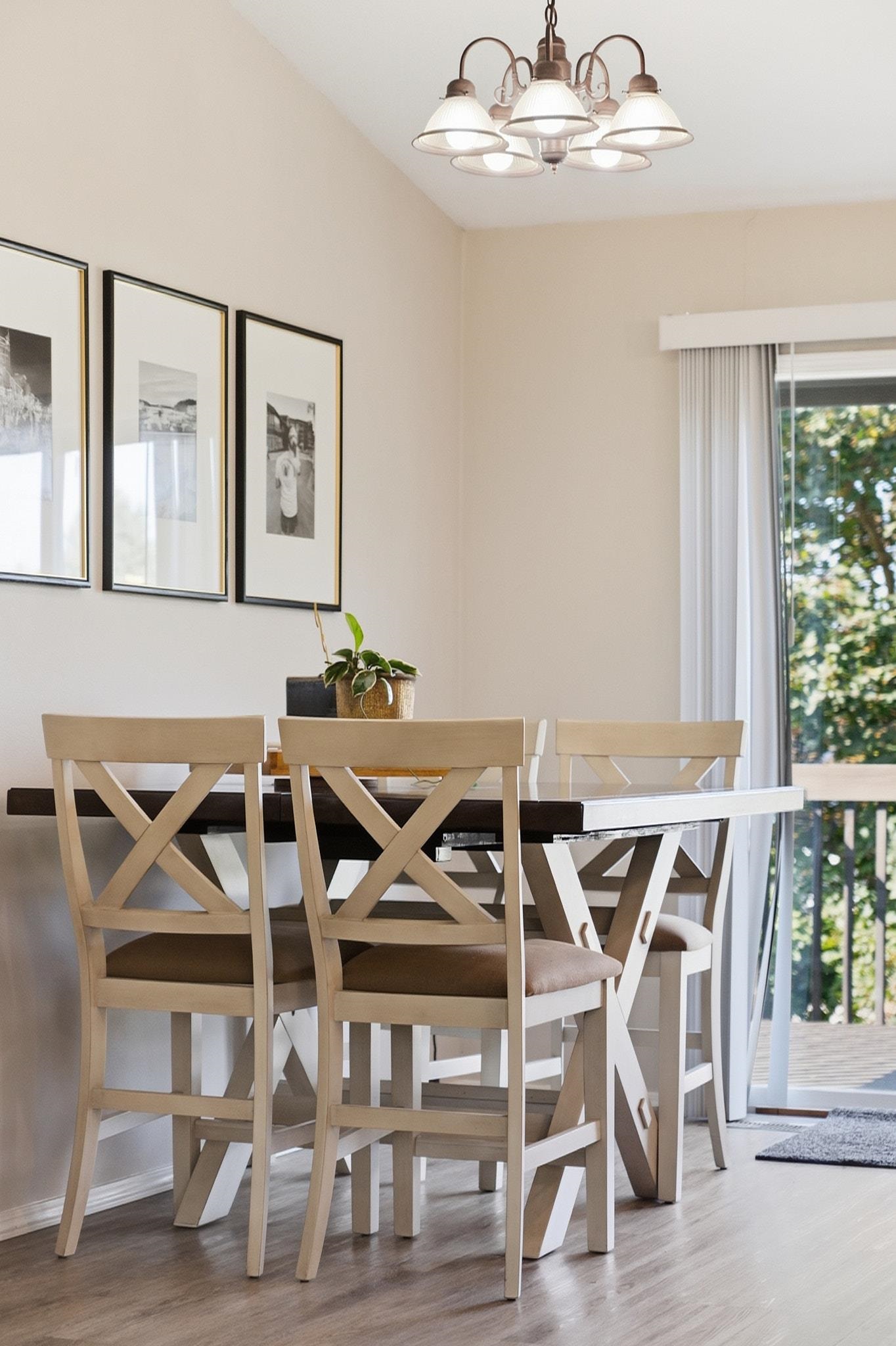 Dining area with a dark table, light cross-back chairs, chandelier, and sliding glass door.