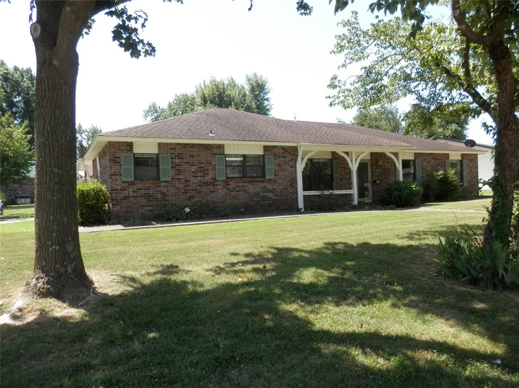 Brick ranch home with a covered entry porch, green shutters, and mature trees framing the lawn.