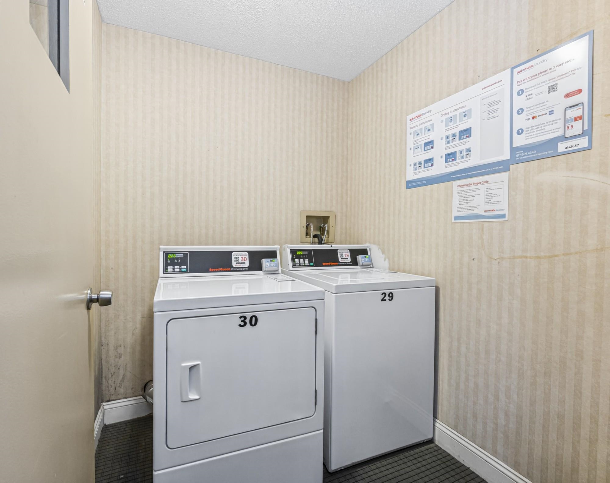 Shared laundry room with two white commercial machines numbered 30 and 29.