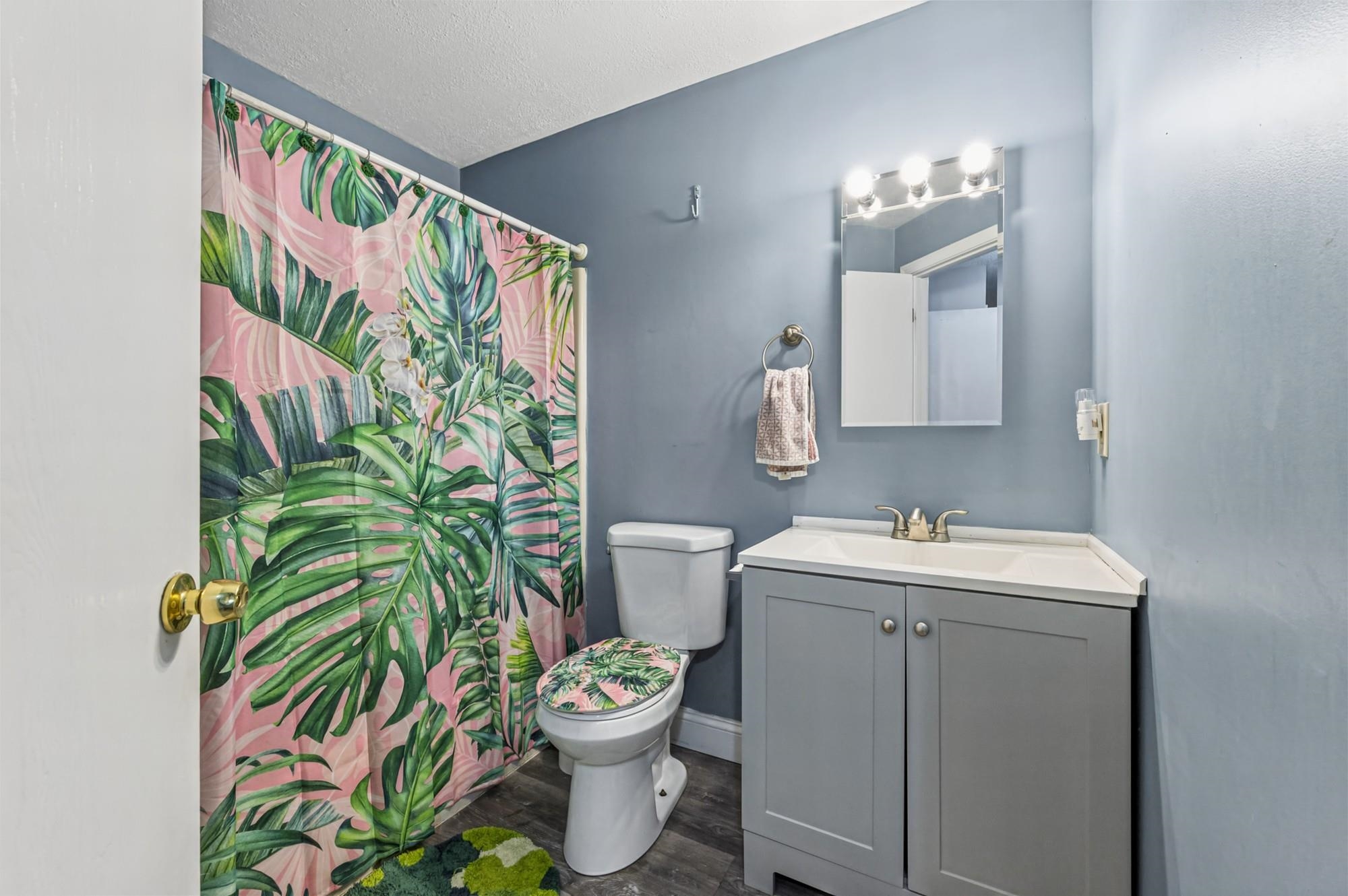 Bathroom with a gray vanity and toilet beside a pink tropical-leaf shower curtain.