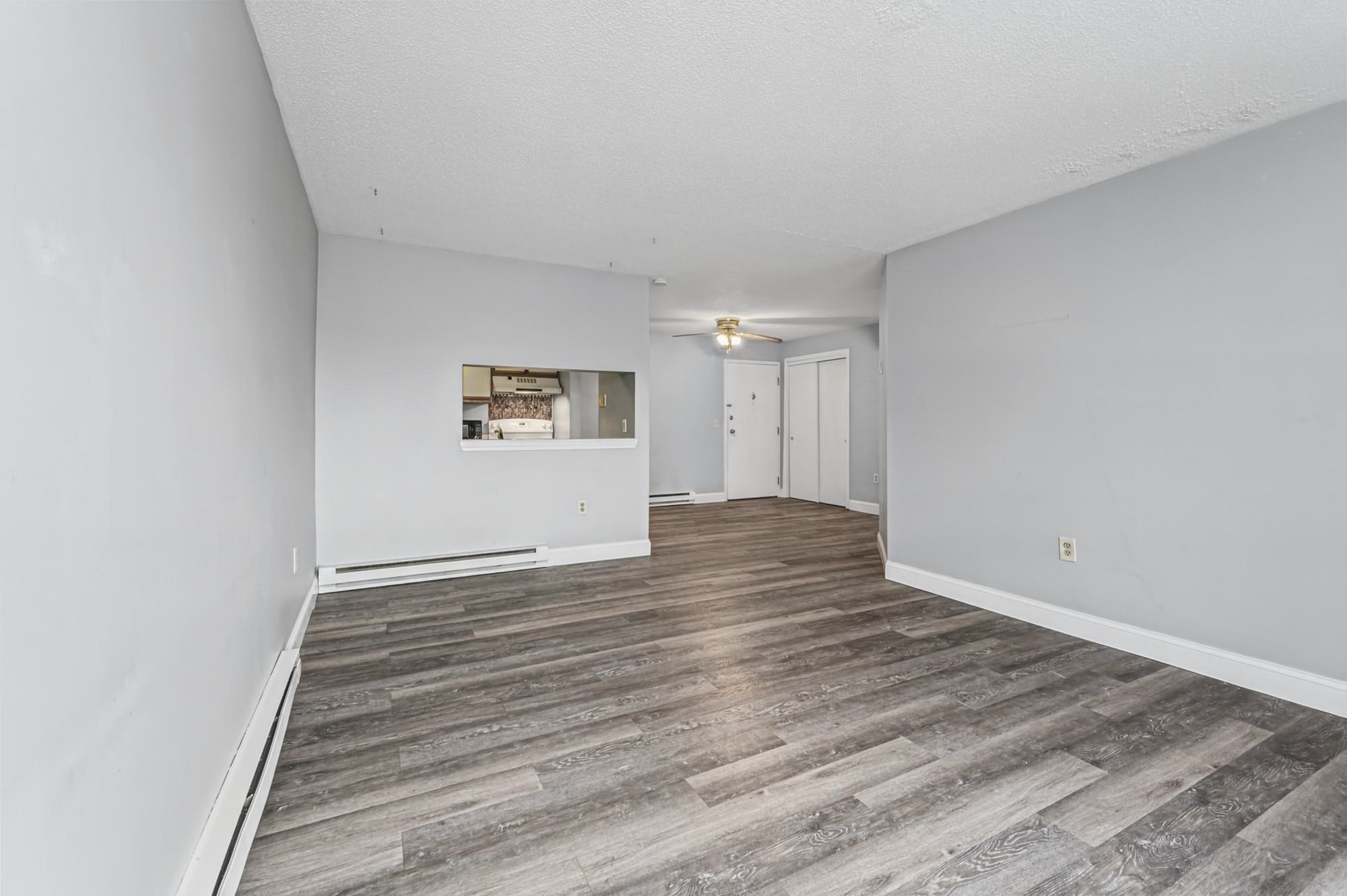 Vacant living room with gray plank flooring, a kitchen pass-through, and a ceiling fan.
