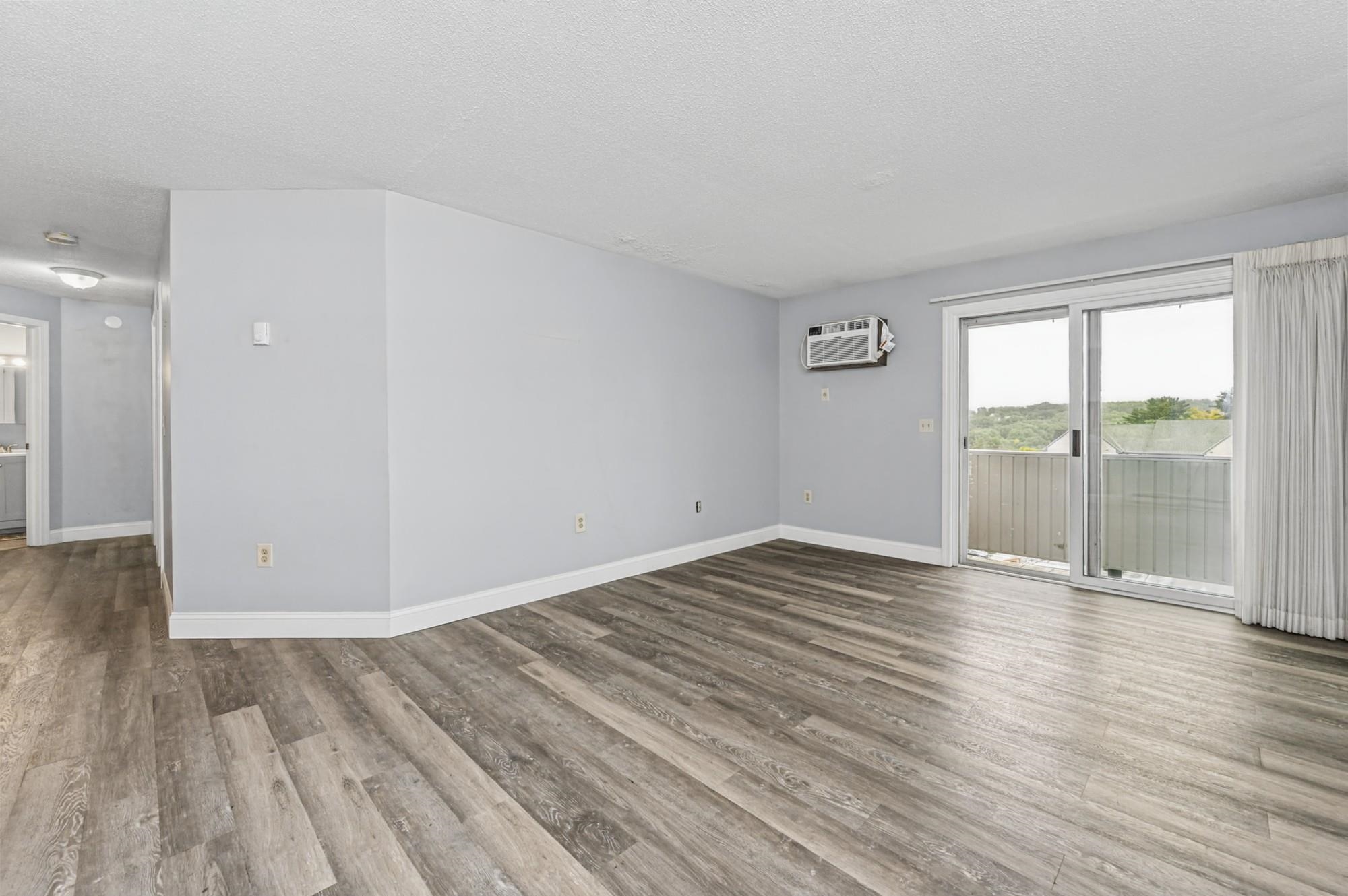Empty living room with plank flooring, a window air conditioner, and sliding doors to a balcony.